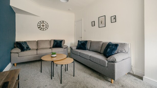 A modern living room with two grey sofas, a round coffee table, and a wall clock. - Canterbury House Horizonstays (Redcar)