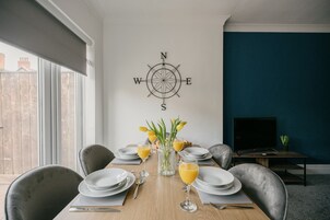 Comedor con decoración de brújula en la pared, una mesa lista para cuatro personas y un televisor al fondo.