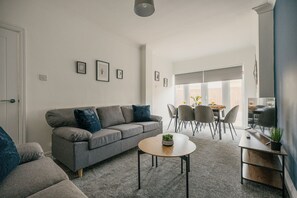 Una sala de estar moderna con un sofá gris, una mesa de centro y un comedor con sillas y una mesa.