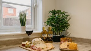 A snack board with cheese, olives, and meats, two bottles of Corona beer, a glass of red wine, and a potted plant on a windowsill. - Canterbury House Horizonstays (Redcar)