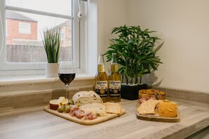 Eine Vorsichtsbrett mit Käse, Oliven und Fleisch, zwei Flaschen Corona Bier, ein Glas Rotwein und ein Topf mit einer Pflanze auf einem Fensterbrett.