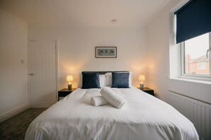 A hotel room with a bed, two bedside lamps, a framed picture on the wall, and a window with a blind. - Canterbury House Horizonstays (Redcar)