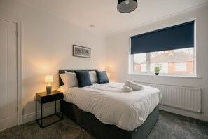 A bedroom with a bed, a nightstand, a lamp, a window with a view, and a picture on the wall. - Canterbury House Horizonstays (Redcar)