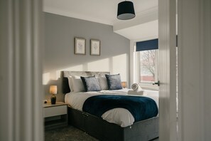 Um quarto com uma cama, mesas de cabeceira, uma luminária e duas imagens emolduradas na parede.