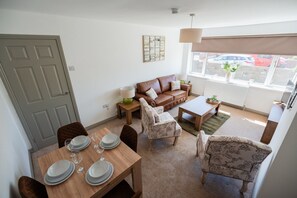 Ein Wohnzimmer mit einer Couch, einem Esstisch für vier Personen und einem Fenster mit Blick auf die Straße.