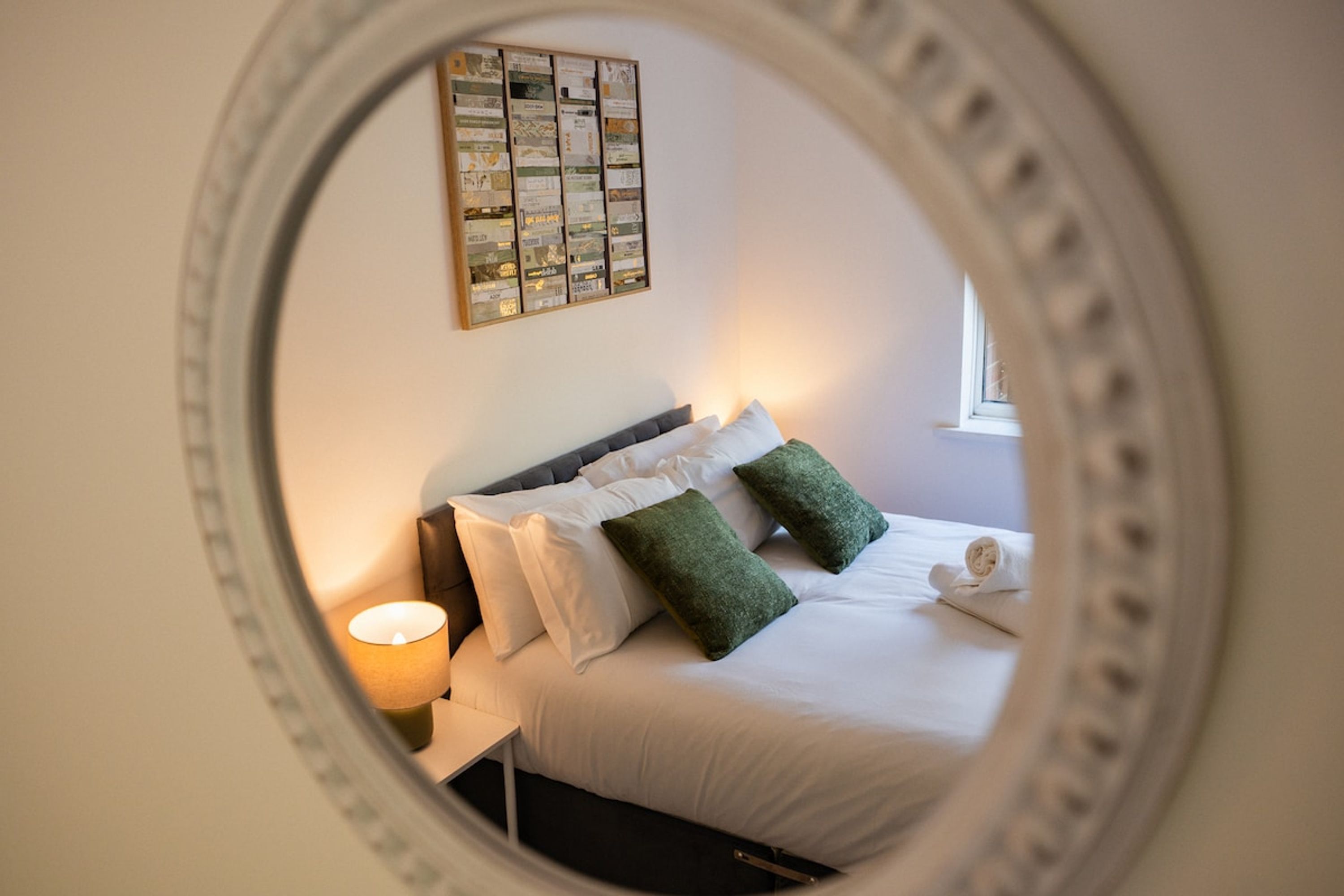 Ein Schlafzimmer mit einem Bett, Kissen, einem Nachttisch, einer Lampe und einem Wandbild.