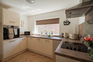 Eine kleine Küche mit Mikrowelle, Toaster und Wasserkocher auf der Arbeitsfläche, ein Fenster mit Blick auf eine Ziegelwand und einer Wandhalterung für eine Kaffeetasse.