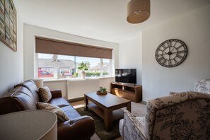 A living room with a sofa, a coffee table, a TV, and a clock on the wall. - Winston Bungalow By Horizon Stay (Middlesbrough)