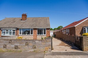 A two-story brick house with a tiled roof, a stone wall with decorative cut-outs, and a gated driveway. - Winston Bungalow By Horizon Stay (Middlesbrough)