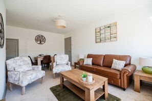 A living room with a brown leather sofa, two patterned armchairs, a wooden coffee table, and a dining area with a table and chairs. - Winston Bungalow By Horizon Stay (Middlesbrough)