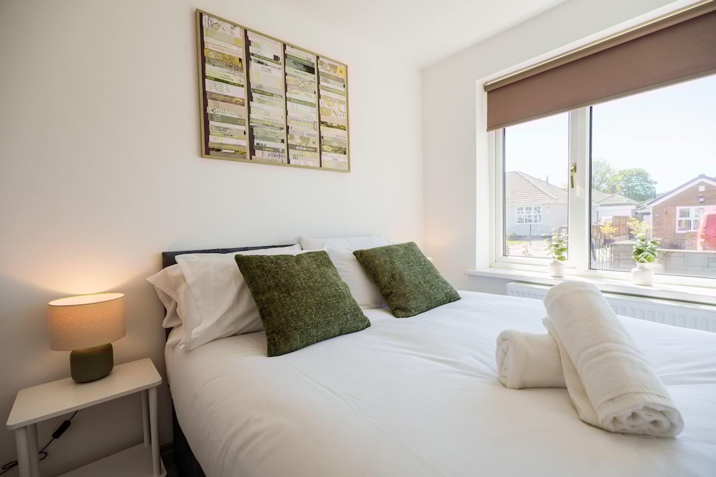 Une chambre d’hôtel avec un lit bien fait, une table de chevet avec une lampe et une fenêtre donnant sur les bâtiments environnants.