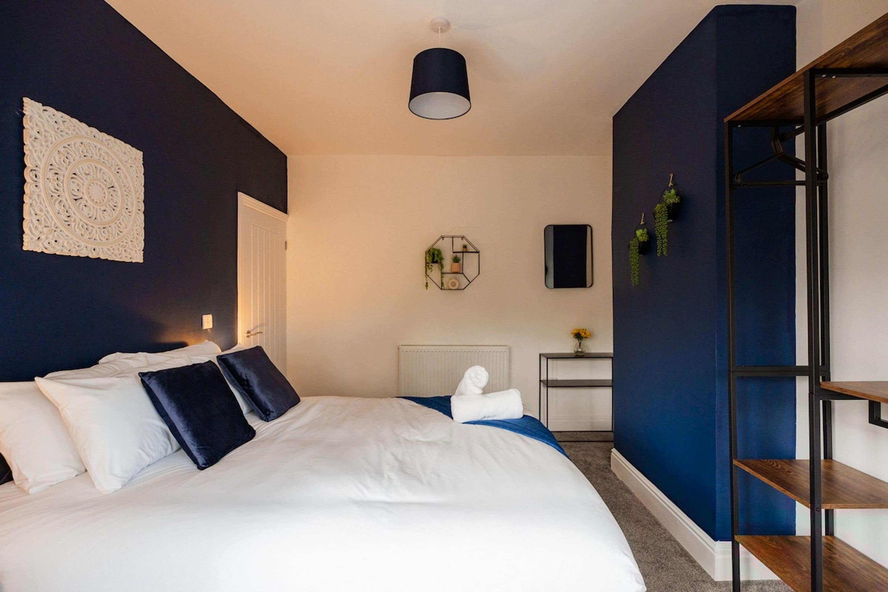 A modern hotel room with a large bed, a bedside table, a mirror, and a blue accent wall.