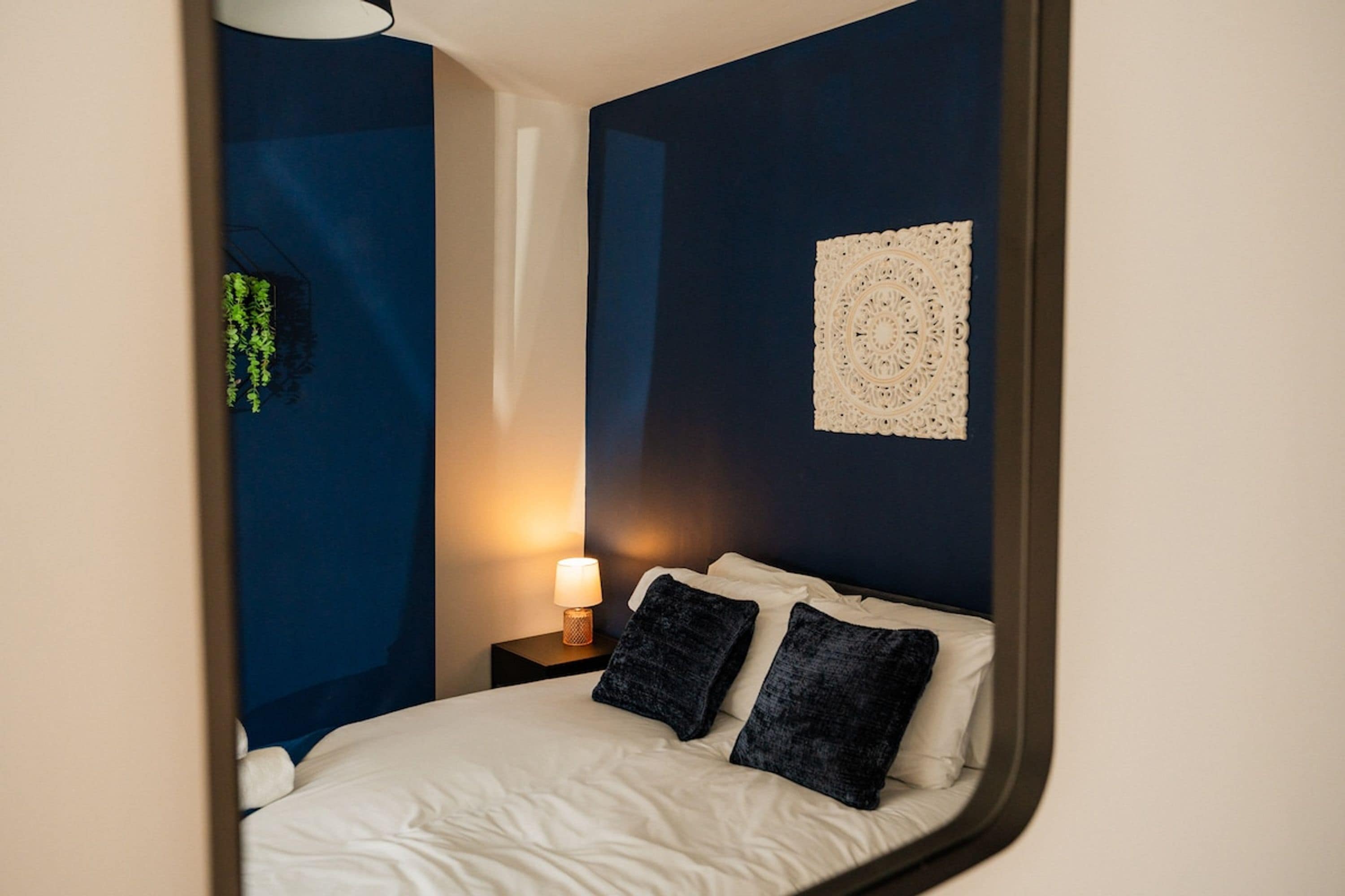 A bedroom with a bed, a nightstand, a wall-mounted lamp, and a wall decoration.