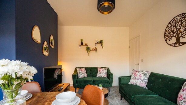 A living room with a green sofa, a wooden dining table with white plates, and a vase of white flowers. - Redcar House Horizon Stays (Redcar)