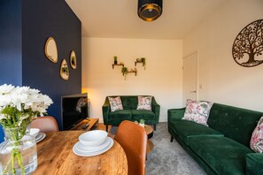 Ein Wohnzimmer mit einem grünen Sofa, einem Holztisch mit weißen Tellern und einer Vase mit weißen Blumen.