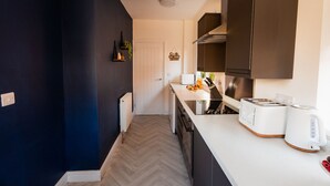 A modern kitchen with a herringbone floor, dark cabinetry, and a white countertop. - Redcar House Horizon Stays (Redcar)
