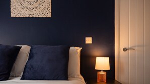 A bedroom with a bed, pillows, a nightstand with a lamp, and a wall-mounted light switch. - Redcar House Horizon Stays (Redcar)