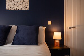 A bedroom with a bed, pillows, a nightstand with a lamp, and a wall-mounted light switch. - Redcar House Horizon Stays (Redcar)