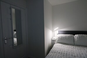 A bedroom with a bed, a bedside table, a lamp, and a door. - Hillwood Court Central Thornaby (Stockton-on-Tees)