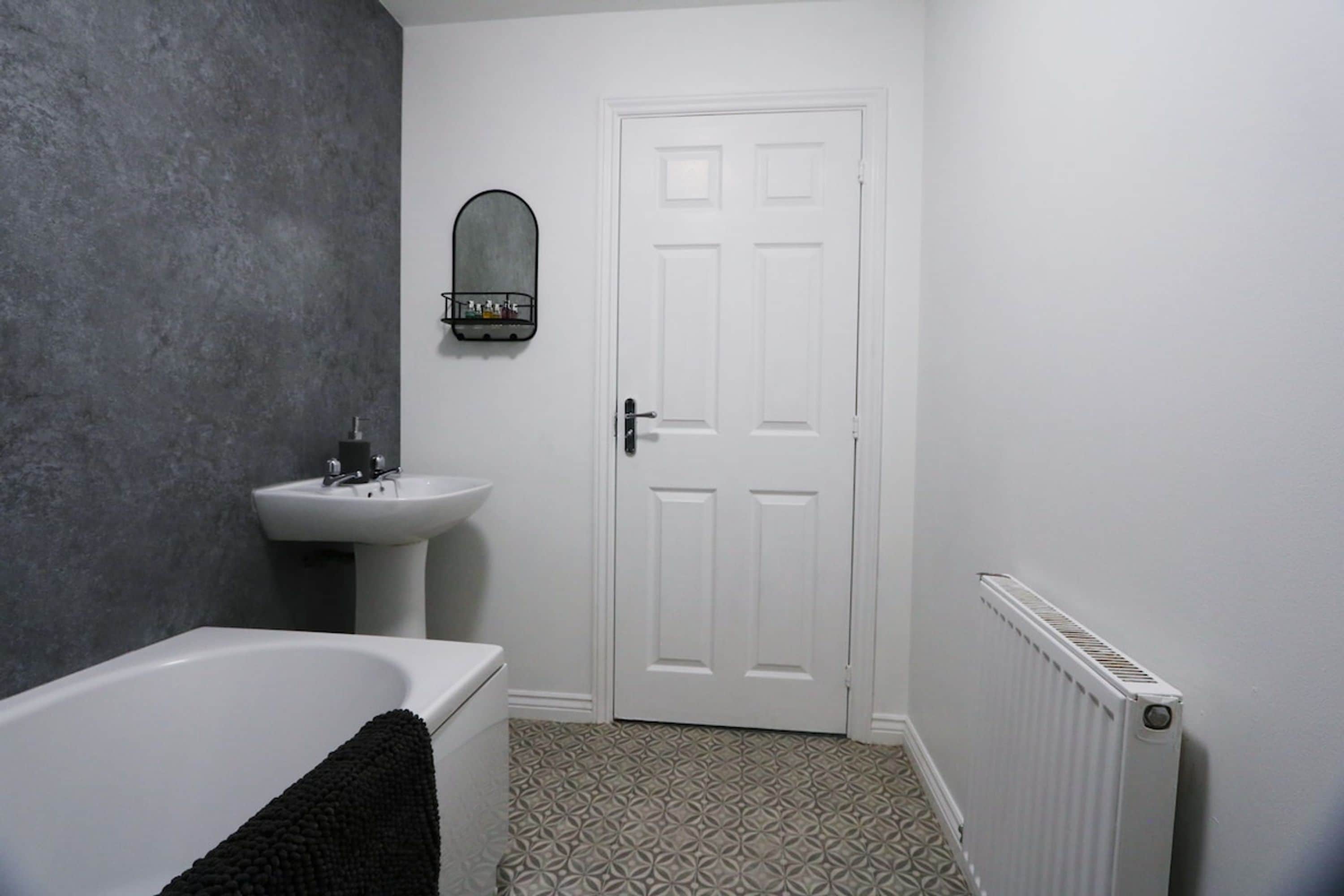 A bathroom with a white bathtub, a white sink, a mirror, and a door.