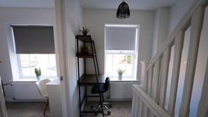 Ett rum med ett skrivbord, en stol, en hyllsektion och två fönster med persienner.