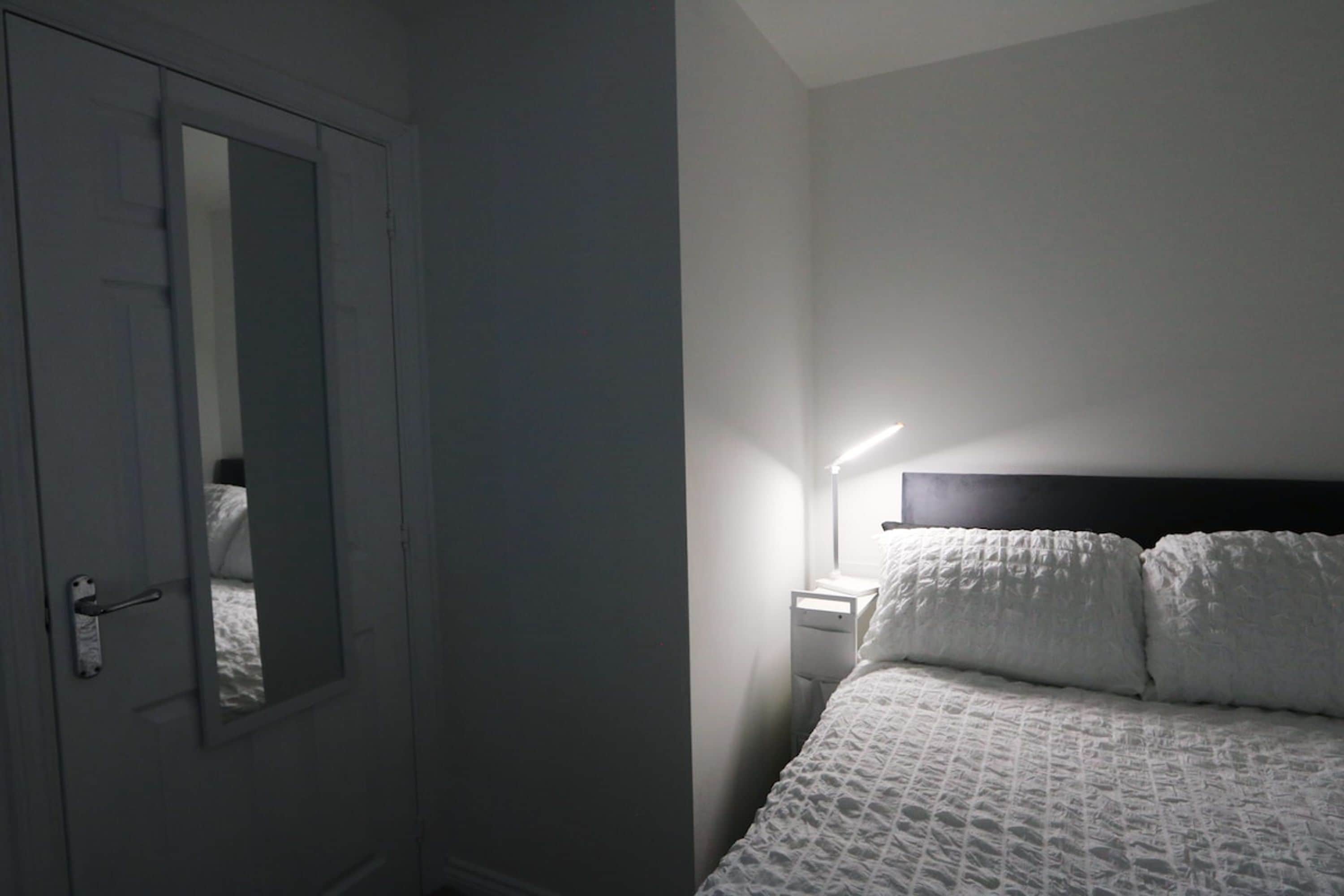 A bedroom with a bed, a bedside table, a lamp, and a door.