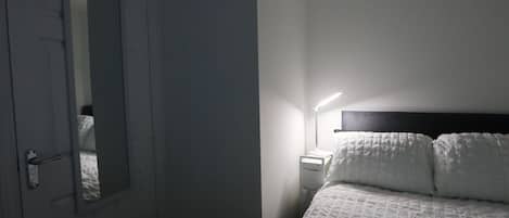 A bedroom with a bed, a bedside table, a lamp, and a door.