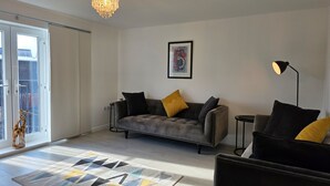 Ett modernt vardagsrum med en grå soffa, en svart golvlampa och en mönstrad matta.