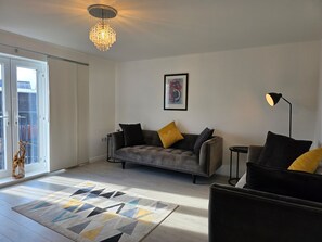 Ein modernes Wohnzimmer mit einem grauen Sofa, einer schwarzen Stehlampe und einem gemusterten Teppich.