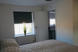 A bedroom with a bed, a window with a plant, a door, and a bathroom with a sink. - Hillwood Court Central Thornaby (Stockton-on-Tees)