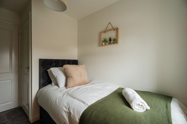 A neatly made bed with a headboard, a bedside table, and a wall-mounted plant. - Babbage House Horizon Stays (Stockton-on-Tees)