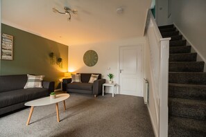 A living room with a sofa, a coffee table, a clock, and a staircase. - Babbage House Horizon Stays (Stockton-on-Tees)