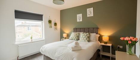 A bedroom with a bed, bedside lamps, a window, and a view of buildings outside.