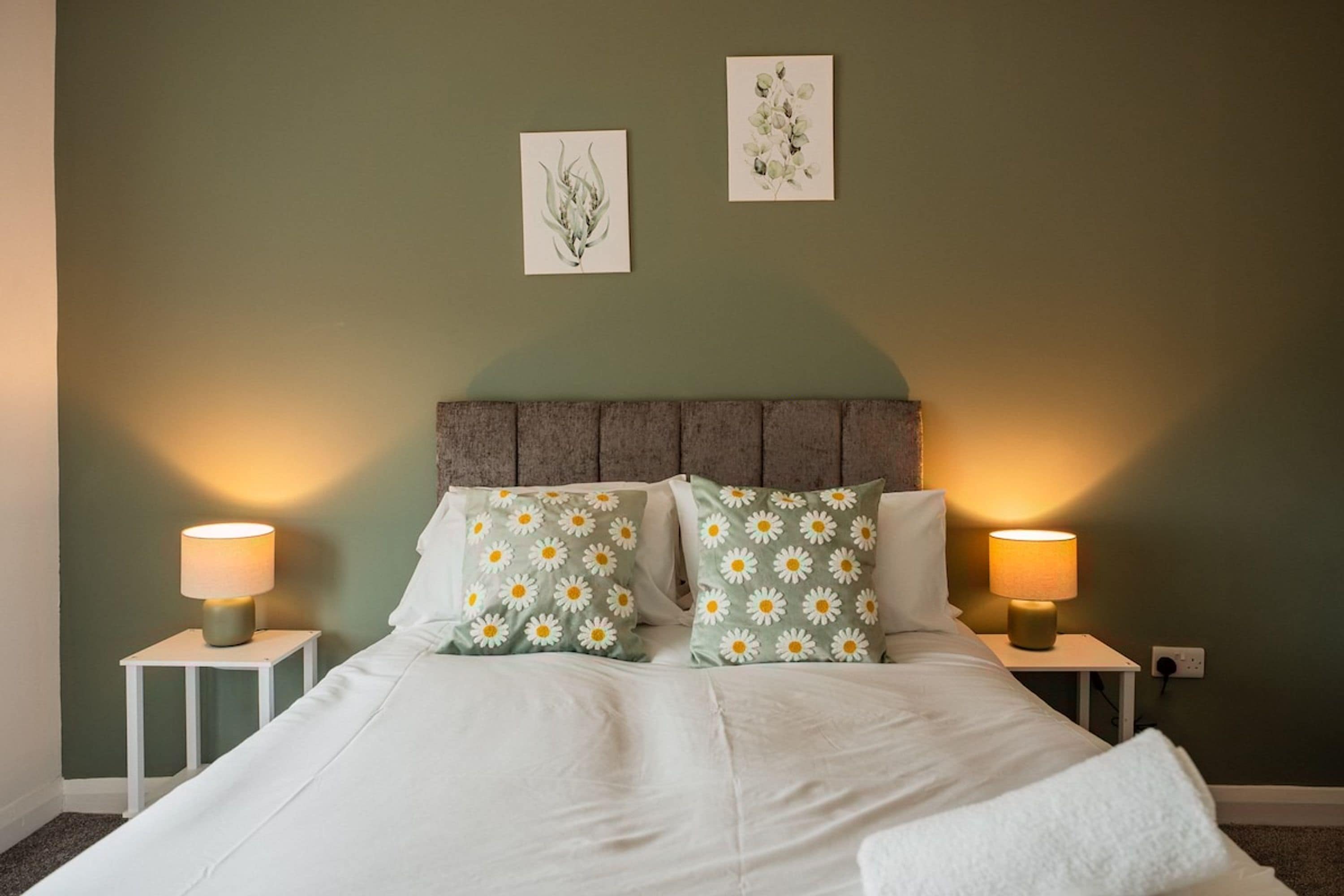 A bed with two pillows, two bedside tables, and two wall-mounted lamps.