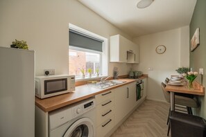 A compact kitchen with a washing machine, microwave, and a window with potted plants. - Laburnum House by Horizon Stays (Redcar)