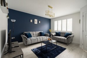 Ein modernes Wohnzimmer mit zwei Sofas, einem Couchtisch, einer Stehlampe und einem großen Fenster mit Jalousien.