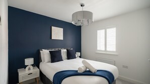 Ein Schlafzimmer mit einem Bett, Nachttischen, einem Fenster mit Jalousien und einer Deckenleuchte.
