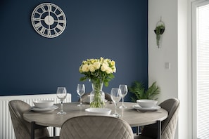 A dining table with white plates and glasses, a vase with flowers, and a wall clock. - Gibson House Horizon Stays (Stockton-on-Tees)
