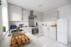 Une cuisine moderne avec des meubles blancs, une hotte en acier inoxydable, un four encastré, un four à micro-ondes et un réfrigérateur.