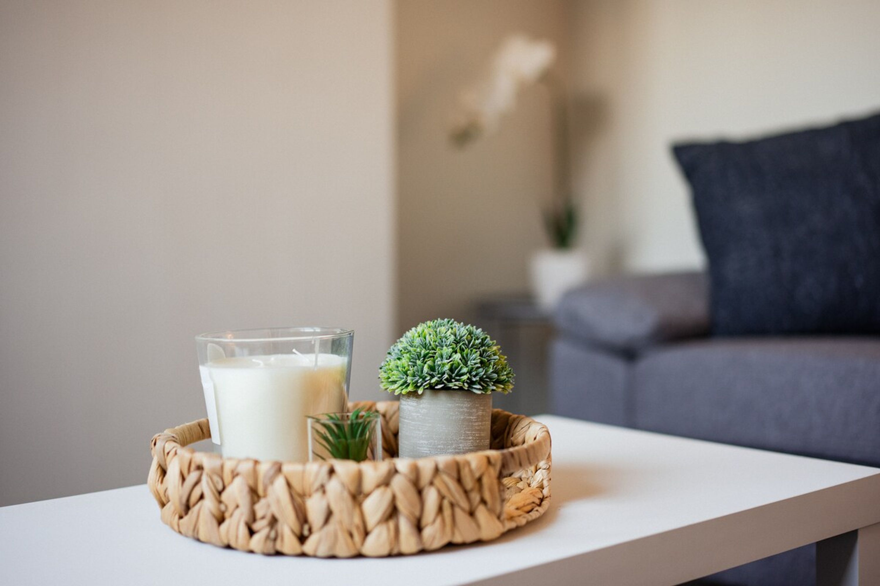 A table with a woven tray holding a glass of milk, a small potted plant, and a candle.