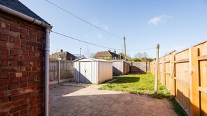 Un muro de ladrillo, un patio empedrado y una valla de madera en un jardín trasero residencial.