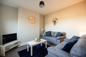A living room with a flat-screen TV, a white coffee table, a grey sofa, and a blue rug. - Westbourne House Horizon Stays (Middlesbrough)
