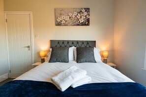 Una habitación de hotel con una cama, dos lámparas de noche, un cuadro en la pared y una puerta.
