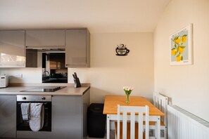 A compact kitchen with modern appliances, a dining area with a white table and chair, and a wall-mounted artwork of lemons. - Westbourne House Horizon Stays (Middlesbrough)