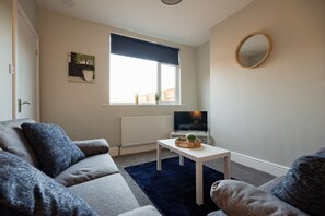 Una sala de estar con sofá, mesa de centro, televisor y ventana con vistas.