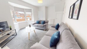 Ein modernes Wohnzimmer mit einem grauen Sofa, einem kleinen runden Tisch und einem Fernseher.