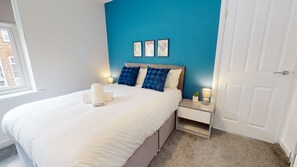 Ein Schlafzimmer mit einem Bett, Nachttischen, einer Tür und einem Fenster.