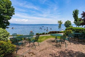 A patio with green metal chairs and tables overlooking a lake with boats. - Gilford Lake Retreat • 5-Min Walk to Beach • Pool (Gilford)
