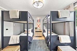 Ein Schlafraum mit Etagenbetten, einem Nachttisch in der Mitte, einem gerahmten Bild und einem Fenster mit Vorhängen.