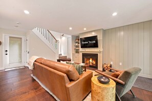 Ein Wohnzimmer mit Ledersofa, Couchtisch aus Holz, Kamin und Wandfernseher.